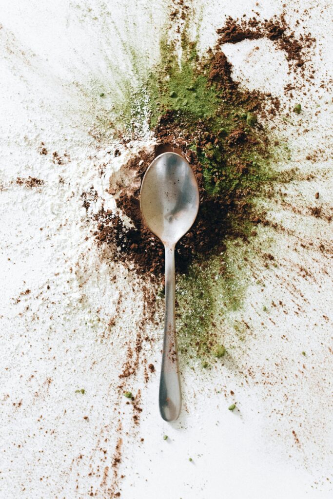 Top view of a spoon amidst a vibrant array of spices scattered on a white surface.
