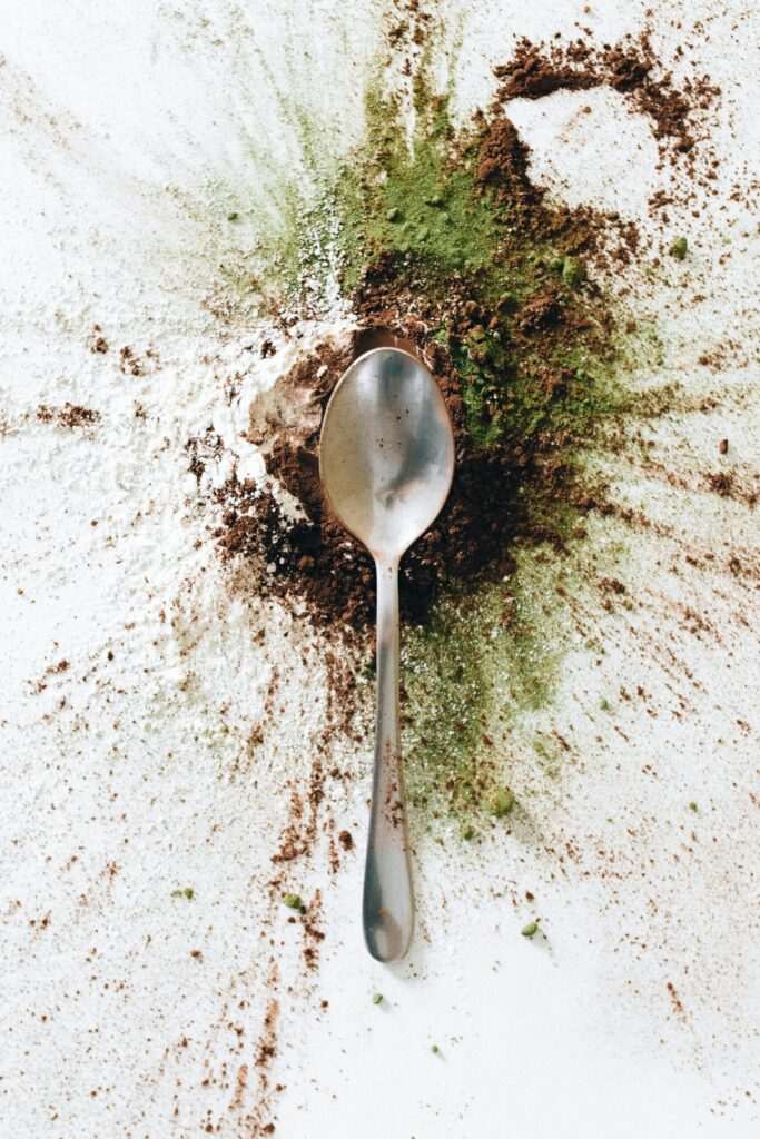 Top view of a spoon amidst a vibrant array of spices scattered on a white surface.