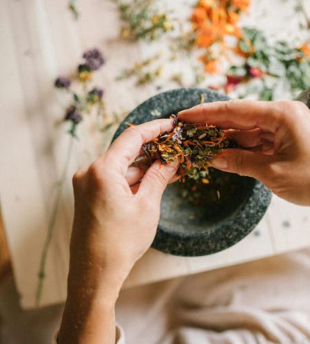 Close-up of hands mixing dried herbs with a mortar and pestle for herbal medicine preparation.